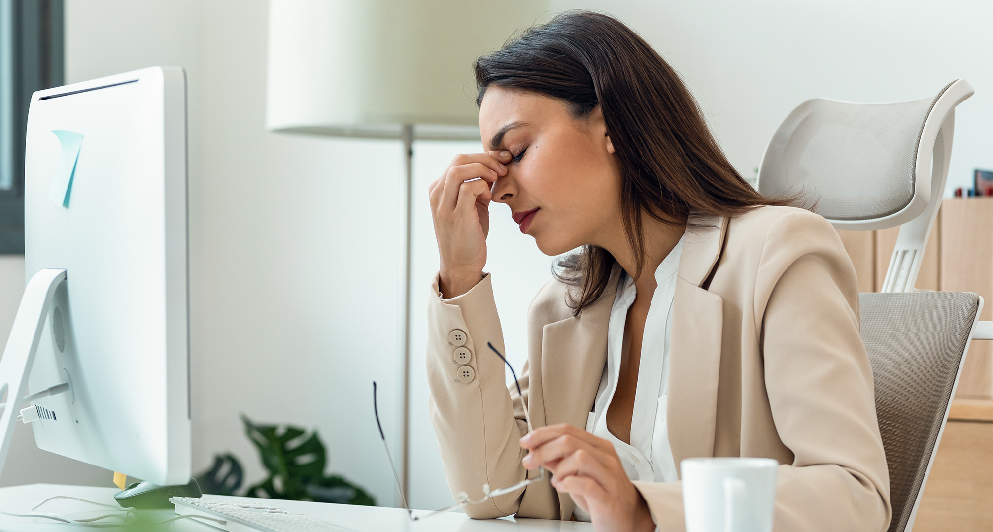 persona che strizza gli occhi per affaticamento oculare, seduta alla scrivania con gli occhiali