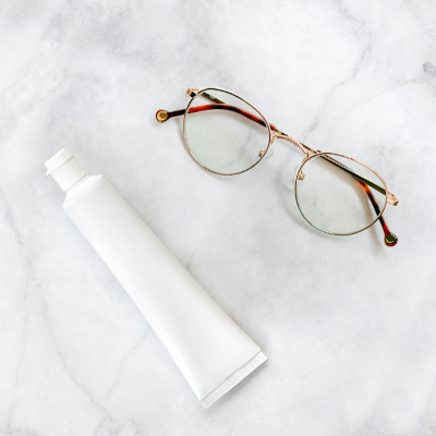 Tubo di dentifricio bianco e occhiali con montatura a filo su sfondo neutro